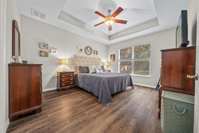 bedroom with ceiling fan, a tray ceiling, and dark hardwood / wood-style flooring