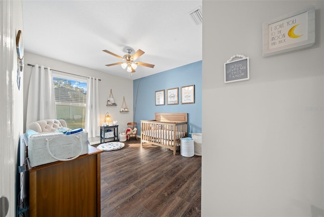 bedroom with a nursery area, ceiling fan, and hardwood / wood-style flooring