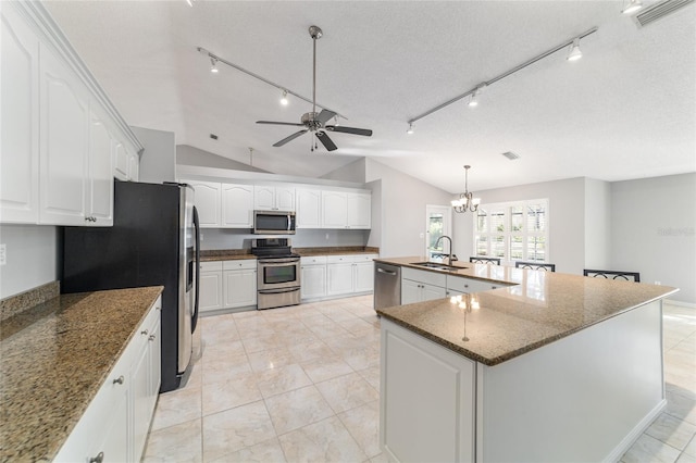 kitchen with appliances with stainless steel finishes, a kitchen island with sink, hanging light fixtures, white cabinetry, and vaulted ceiling