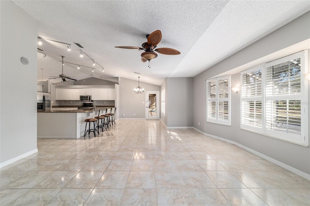 unfurnished living room featuring light tile patterned floors, ceiling fan with notable chandelier, vaulted ceiling, and a textured ceiling