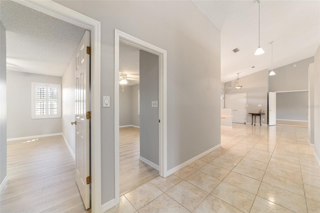 hall featuring high vaulted ceiling, light tile patterned floors, and a textured ceiling