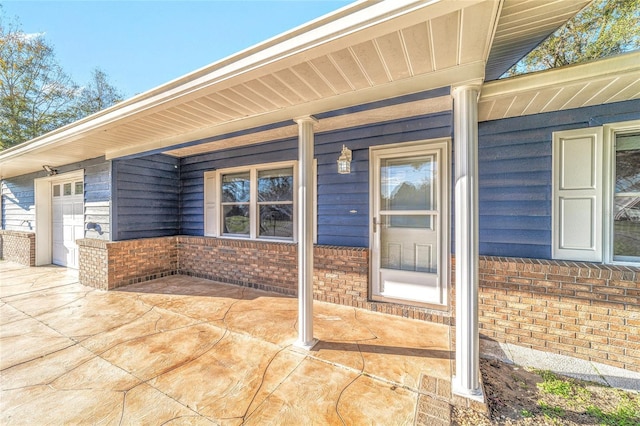 view of exterior entry with covered porch, brick siding, and an attached garage