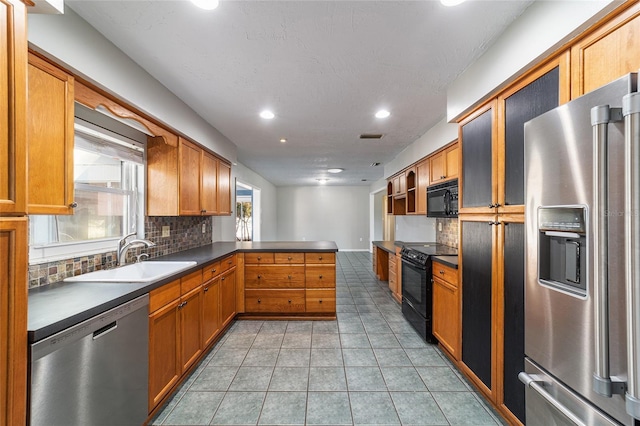 kitchen with light tile patterned floors, a peninsula, a sink, black appliances, and dark countertops