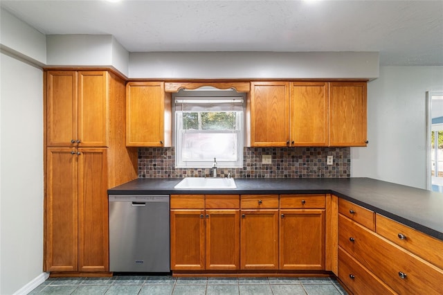 kitchen featuring brown cabinets, tasteful backsplash, dark countertops, stainless steel dishwasher, and a sink