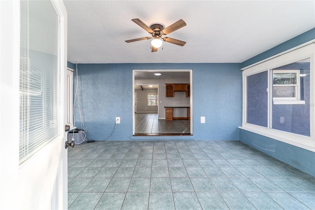 spare room featuring tile patterned floors, a ceiling fan, and a textured wall