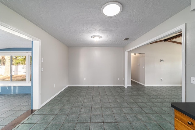 spare room featuring a textured ceiling, lofted ceiling with beams, dark tile patterned floors, visible vents, and baseboards