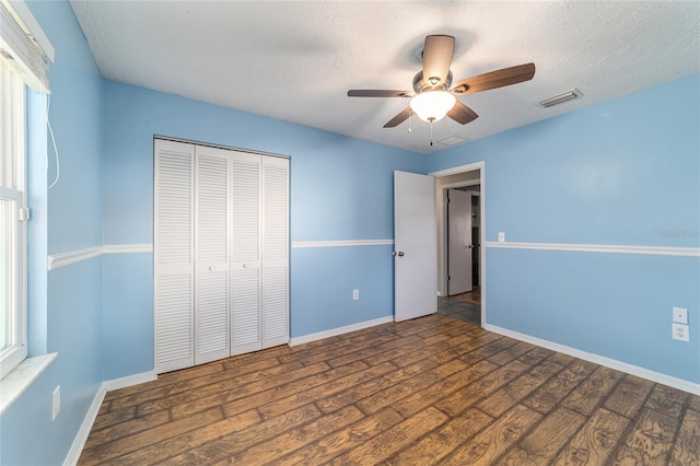 unfurnished bedroom featuring a closet, visible vents, a textured ceiling, wood finished floors, and baseboards