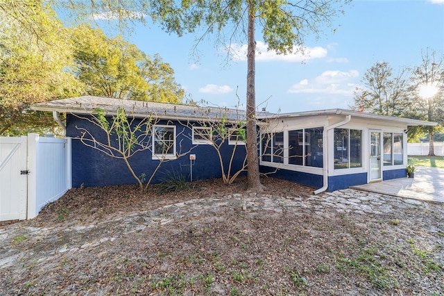 rear view of property featuring a sunroom, a gate, fence, and stucco siding