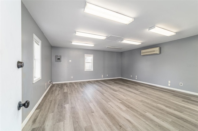 unfurnished room with light wood finished floors, a wall mounted air conditioner, and baseboards