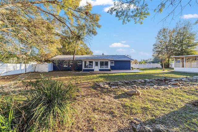 ranch-style home with a front yard, a sunroom, a fenced backyard, and a patio area