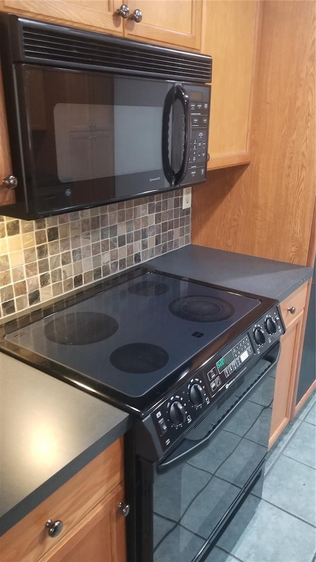 kitchen featuring light tile patterned floors, black appliances, dark countertops, and backsplash