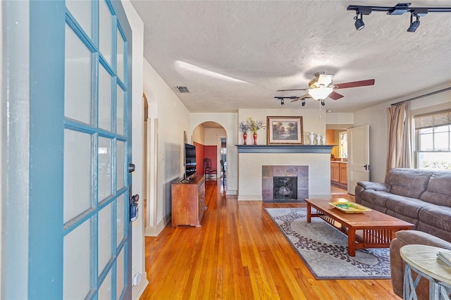 living room featuring ceiling fan, hardwood / wood-style flooring, a tile fireplace, and a textured ceiling