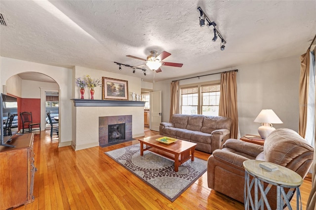 living room with ceiling fan, a fireplace, a textured ceiling, and light wood-type flooring