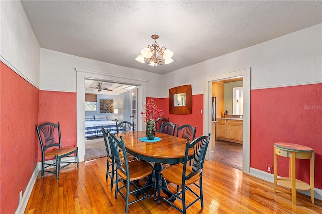 dining area featuring light wood-type flooring, a textured ceiling, and a notable chandelier