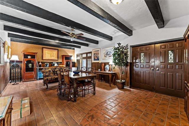 dining area with ceiling fan, wood walls, wainscoting, beamed ceiling, and dark wood finished floors