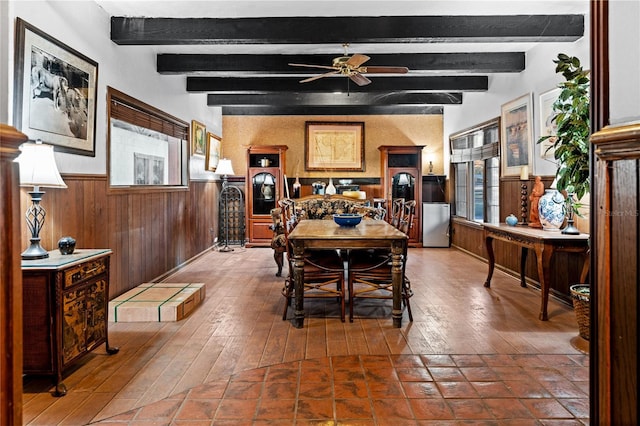 dining room featuring ceiling fan, wooden walls, a wainscoted wall, wood finished floors, and beamed ceiling