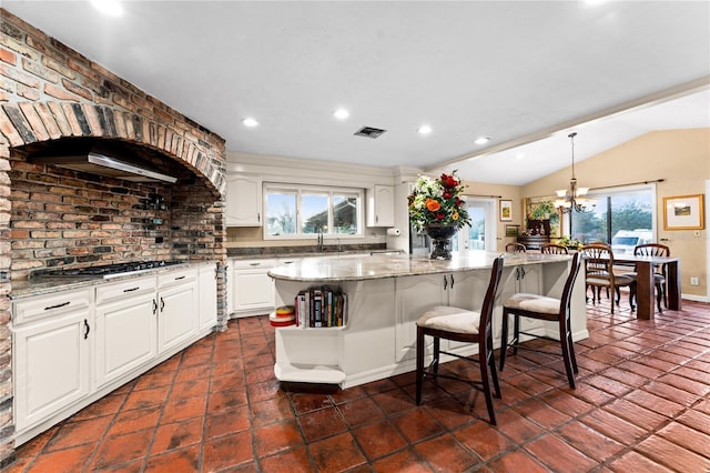 kitchen with light stone counters, visible vents, hanging light fixtures, white cabinets, and a kitchen island