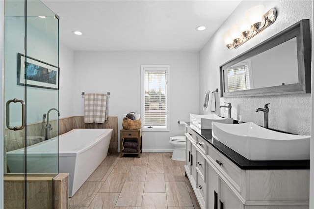 full bathroom featuring a freestanding bath, toilet, vanity, and a wealth of natural light