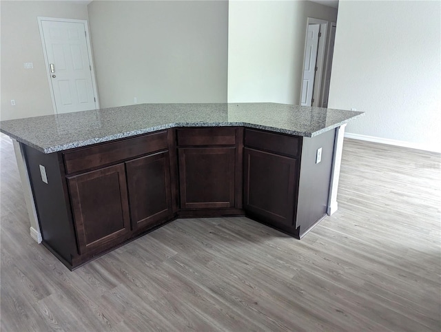 kitchen featuring dark brown cabinets, light stone countertops, a kitchen island, and light wood-type flooring