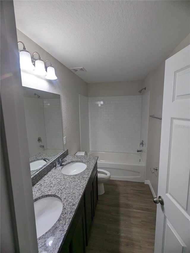 full bathroom featuring toilet, wood-type flooring, a textured ceiling, vanity, and tiled shower / bath combo