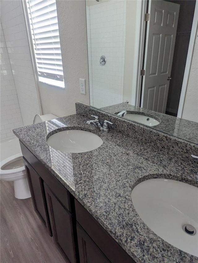 bathroom with a tile shower, vanity, hardwood / wood-style flooring, and toilet