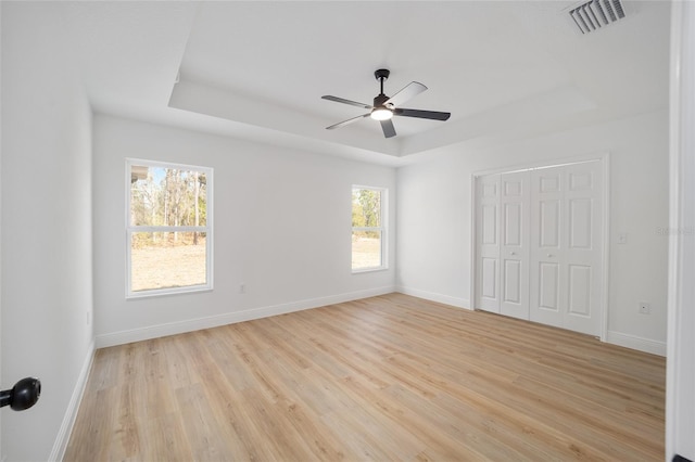 unfurnished room featuring ceiling fan, a tray ceiling, and light hardwood / wood-style floors