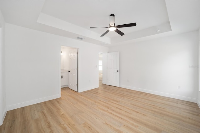 unfurnished bedroom with connected bathroom, light hardwood / wood-style floors, a raised ceiling, and ceiling fan