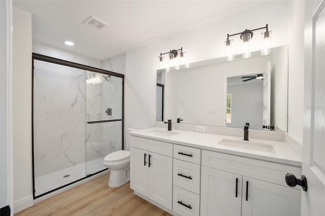 bathroom with toilet, a shower with shower door, wood-type flooring, vanity, and ceiling fan