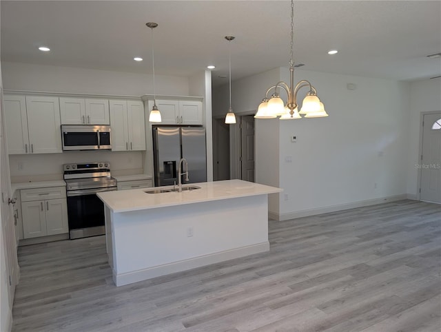 kitchen with white cabinetry, appliances with stainless steel finishes, decorative light fixtures, and a center island with sink