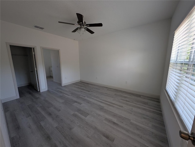 unfurnished bedroom featuring hardwood / wood-style flooring, a walk in closet, ceiling fan, and a closet