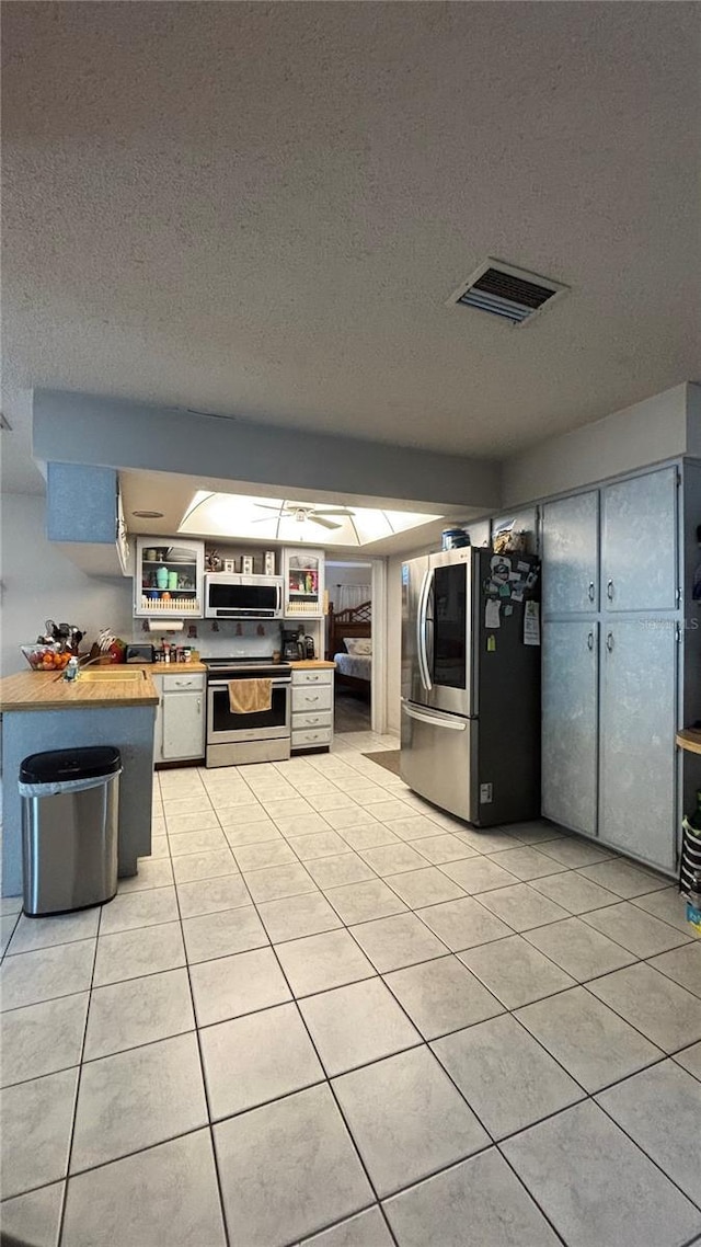 kitchen with appliances with stainless steel finishes, butcher block counters, light tile patterned floors, and a textured ceiling