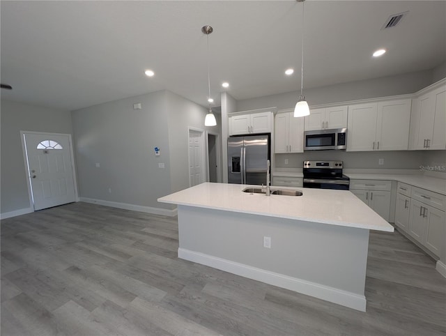 kitchen featuring sink, appliances with stainless steel finishes, hanging light fixtures, white cabinets, and a center island with sink