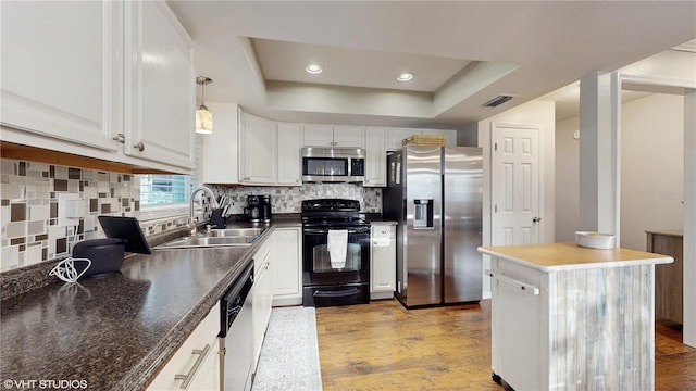 kitchen featuring stainless steel appliances, a sink, white cabinetry, a center island, and a raised ceiling