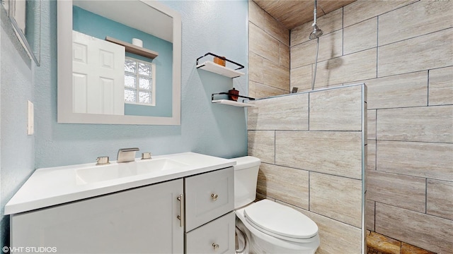 bathroom featuring tiled shower, a textured wall, vanity, and toilet