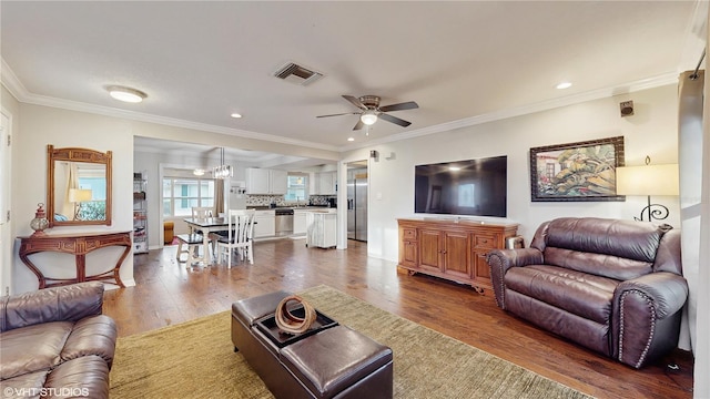 living area featuring visible vents, dark wood-type flooring, crown molding, and a ceiling fan