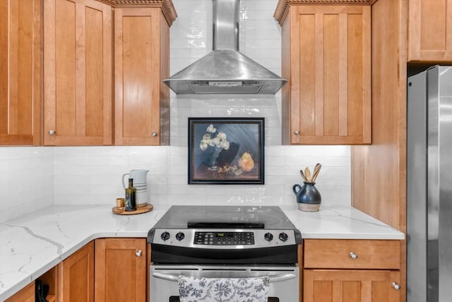 kitchen with tasteful backsplash, appliances with stainless steel finishes, light stone counters, and wall chimney range hood