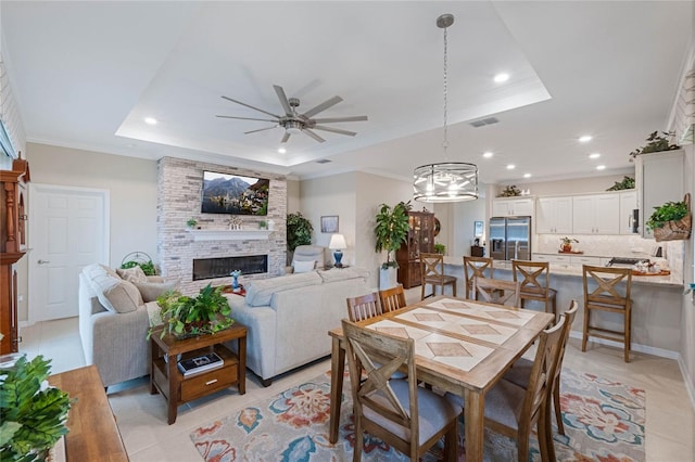 tiled dining space with crown molding, a tray ceiling, a large fireplace, and ceiling fan