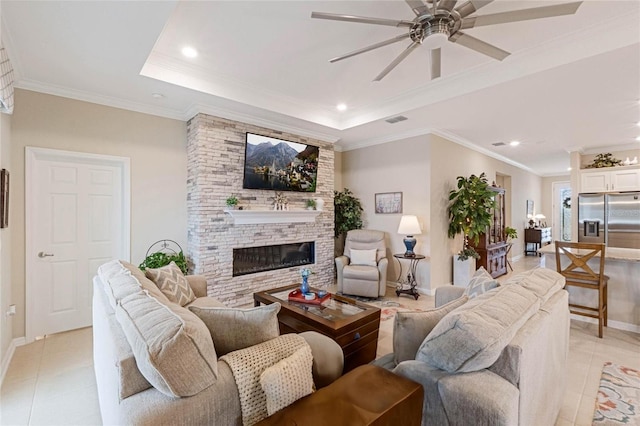 living room featuring light tile patterned flooring, ornamental molding, a stone fireplace, and a raised ceiling