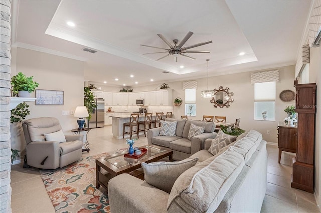 tiled living room with ceiling fan with notable chandelier, ornamental molding, and a raised ceiling