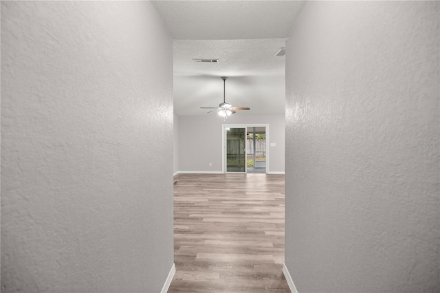 hall with light hardwood / wood-style flooring, a textured ceiling, and vaulted ceiling