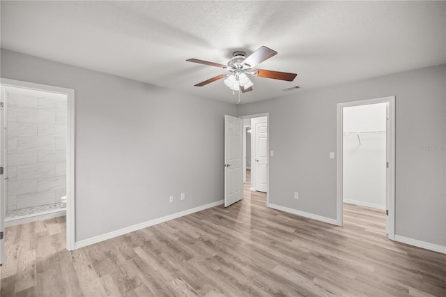 unfurnished bedroom featuring connected bathroom, a spacious closet, light hardwood / wood-style flooring, a textured ceiling, and a closet