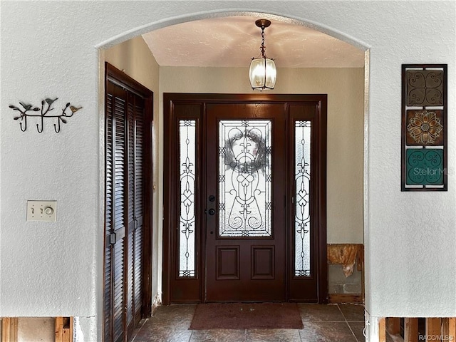 entryway with arched walkways, a textured wall, and stone finish floor