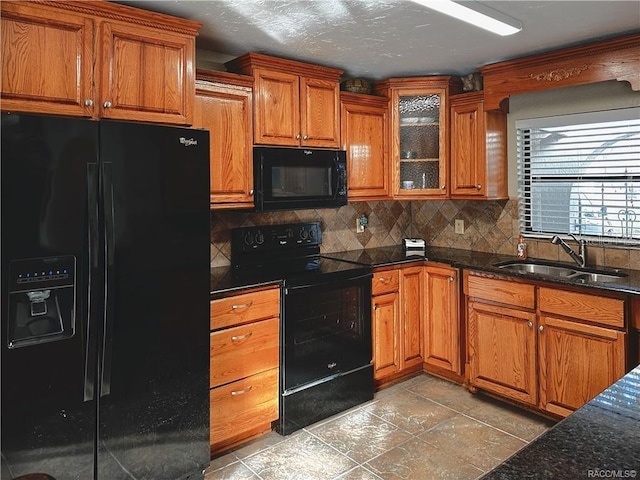 kitchen featuring a sink, decorative backsplash, brown cabinets, black appliances, and glass insert cabinets