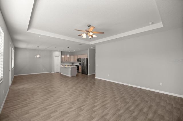 unfurnished living room featuring hardwood / wood-style flooring, ceiling fan, and a tray ceiling