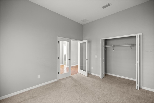 unfurnished bedroom featuring french doors, light colored carpet, and a closet