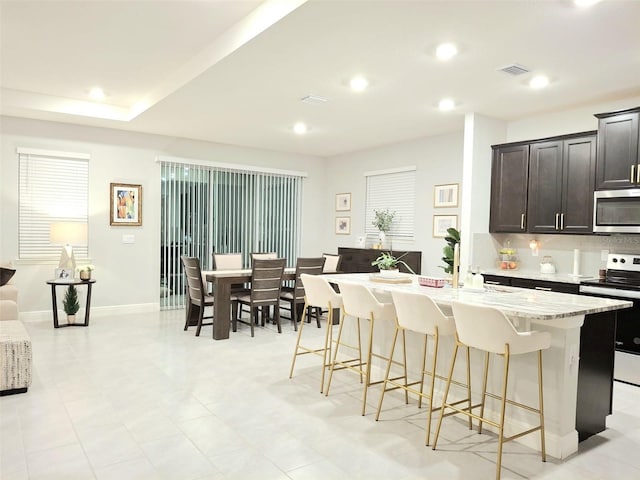 kitchen with appliances with stainless steel finishes, a breakfast bar, decorative backsplash, a kitchen island with sink, and light stone counters