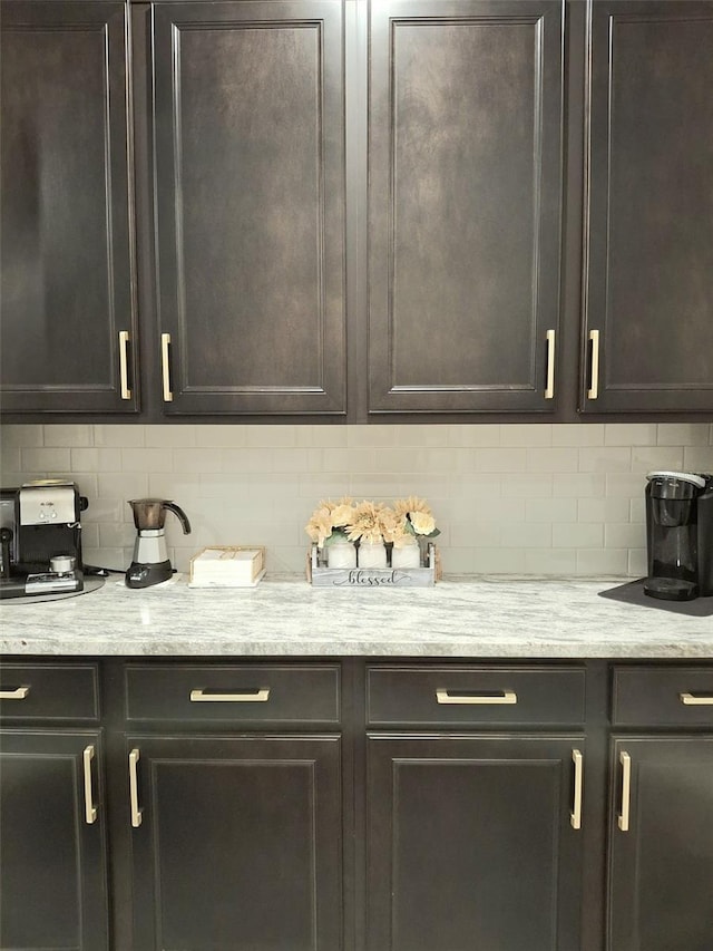 bar with light stone counters, dark brown cabinetry, and backsplash