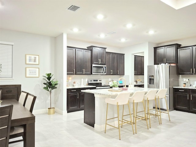 kitchen with dark brown cabinetry, a center island with sink, a breakfast bar area, and appliances with stainless steel finishes