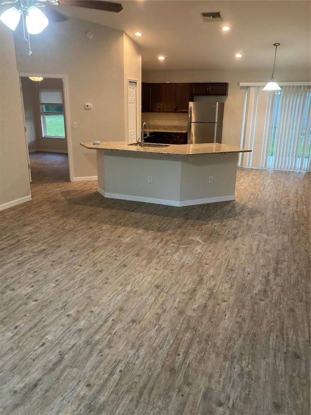 kitchen with sink, hanging light fixtures, stainless steel refrigerator, dark hardwood / wood-style floors, and a kitchen island with sink