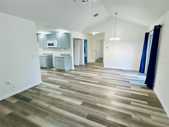 unfurnished living room with ceiling fan with notable chandelier, high vaulted ceiling, and light wood-type flooring